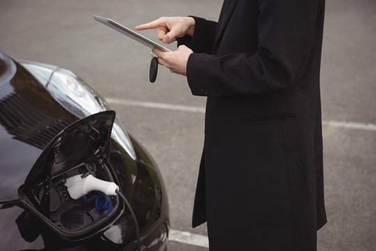 Man using digital tablet while charging electric car