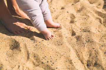 Mother and little baby feet on beach sand.