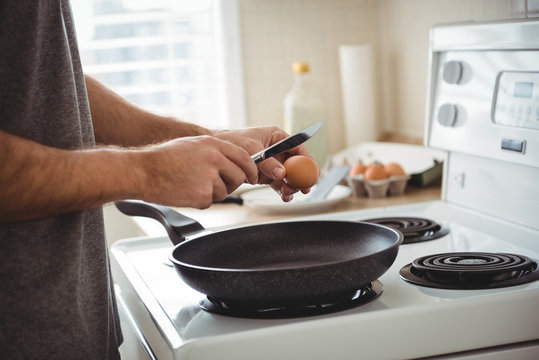 Man cracking an egg into a frying pan in the kitchen