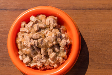 Canned food for cats or dogs in a orange plastic bowl