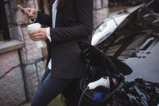Woman using mobile phone while charging electric car