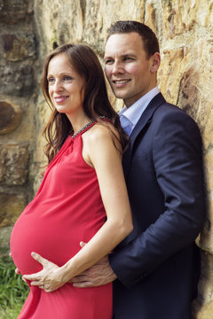 Pregnant woman with husband standing on wall vertical