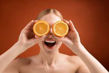 Portrait of happy woman with well cared skin showing two halves of orange. She is looking at camera with joy. Isolated on background