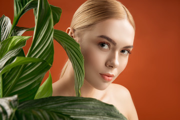 Organic cosmetic concept. Portrait of beautiful girl with pure skin standing near green plant. She...