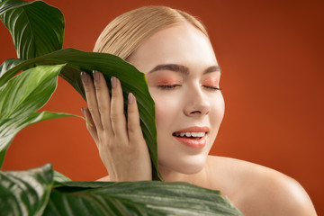 Naturalness concept. Satisfied appealing girl touching green leaves with her cheek. Her eyes are...