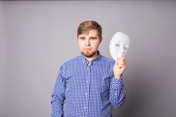 young man taking off plain white mask revealing face, gray background