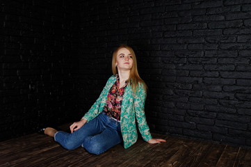 Stylish blonde girl in jacket and jeans against brick black wall at studio.