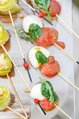 Appetizer, Caprese. Cherry tomatoes,mozzarella and Basil on skewers. . Pesto sauce. Tasty buffet table. Summer party outdoor.