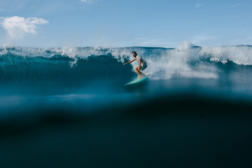 man in wet t-shirt riding big ocean waves on surfboard on sunny day