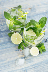 Mojito in two glasses with mint, slices lime, ice cubes, straw on soft blue background, top view, closeup.