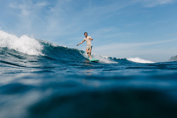 handsome man in wet t-shirt riding waves on surfboard on sunny day