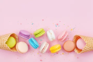 Gordijnen Waffle cone with colorful macaron or macaroon on pink background top view. Flat lay composition. © juliasudnitskaya