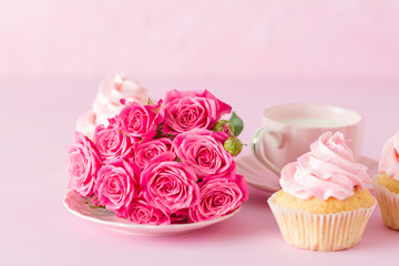 Cupcake with pink cream decoration and roses on pink pastel background.