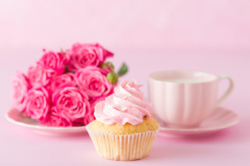 Cupcake with pink cream decoration and roses on pink pastel background.