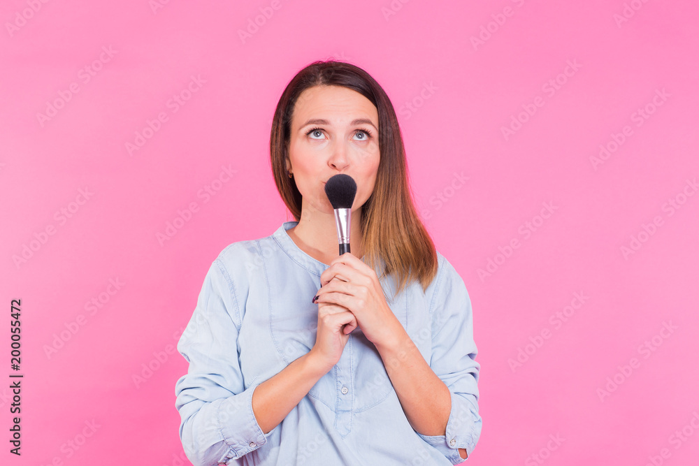 Wall mural Excited beauty makeup artist. Beautiful young woman pretty smiling funny fashion girl holding eyeshadow brushes on pink background