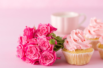 Cupcake with pink cream decoration and roses on pink pastel background.