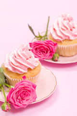 Cupcake with pink cream decoration and roses on pink pastel background.