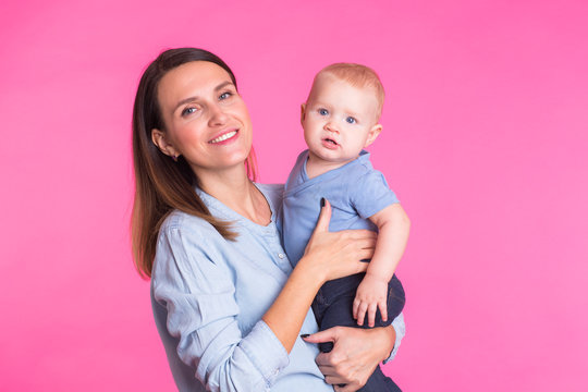 Loving mother playing with her baby boy on pink background