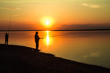  Silhouettes of fishermen against the background of a colorful sunset.