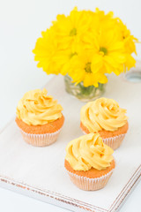 Cupcake with tender yellow cream decoration and bouquet of chrysanthemum in glass on yellow pastel background.