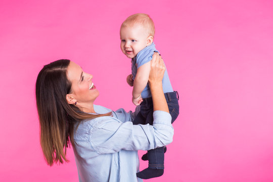 family, motherhood, parenting, people and child care concept - happy mother holds adorable baby over pink background