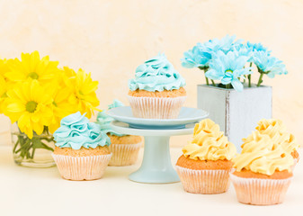 Yellow and blue chrysanthemum in shabby chic vase with cupcakes decorated with tender cream. Copyscape area
