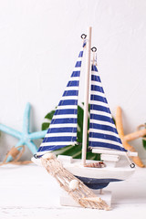 Decorative  wooden toy boat, sea star and tropical plant leaves  on white  textured background.