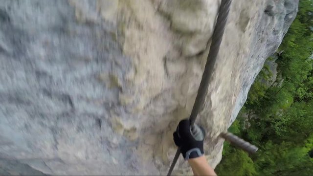 POV - a man climbs up a cliff in a forest using iron pegs