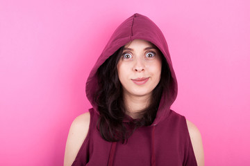 Woman with big eyes wearing a hood on pink background in studio