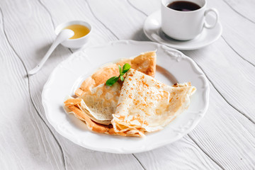 Breakfast pancakes with honey and tea on a white wooden table