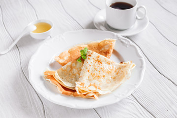 Breakfast pancakes with honey and tea on a white wooden table