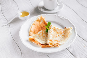 Breakfast pancakes with honey and tea on a white wooden table