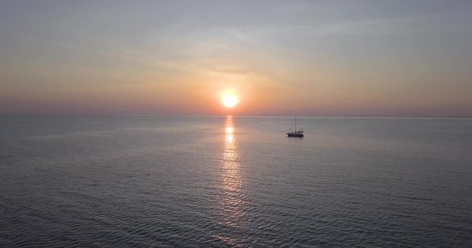 Lone sailboat floats in the ocean under tropical sunset sky. Aerial view.