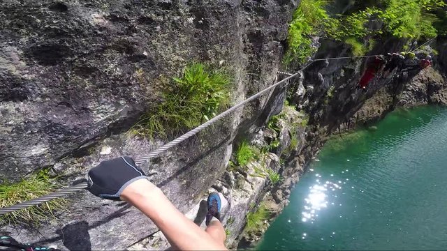 POV - a man climbs alongside a cliff above a river