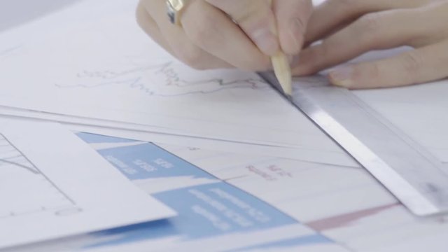 Young professional is drawing on documents sitting in modern office indoors. Male employee works with project documentation at table in architect bureau. Man does job, draws lines on white papers with