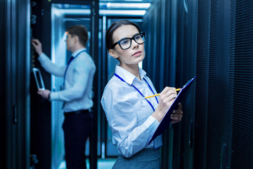 Taking notes. Beautiful determined woman taking notes and her colleague working in the background