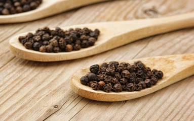 Black pepper in wooden spoon on the old board