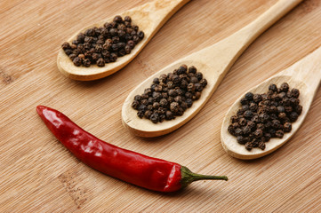 Black and red pepper in wooden spoon on the old board
