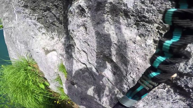 POV - a man climbs alongside a cliff above a river and rearranges the carabiners