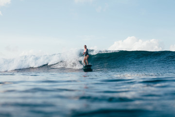 Naklejka premium young woman in wetsuit surfing on sunny day