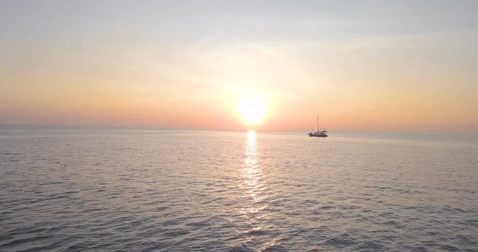 Lone sailboat in the ocean under mesmerizing sunset sky. Aerial shot.
