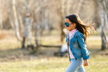 A little girl in a denim suit with long hair runs through the forest
