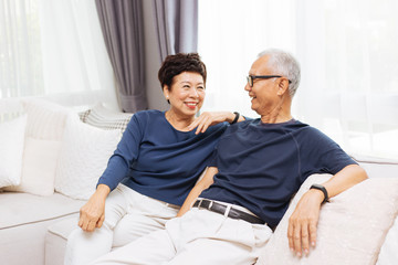 Romantic senior Asian couple laughing and sitting on sofa at home