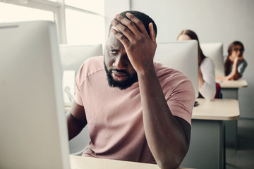 Young afro american man can not decide problem with computer.Sad.