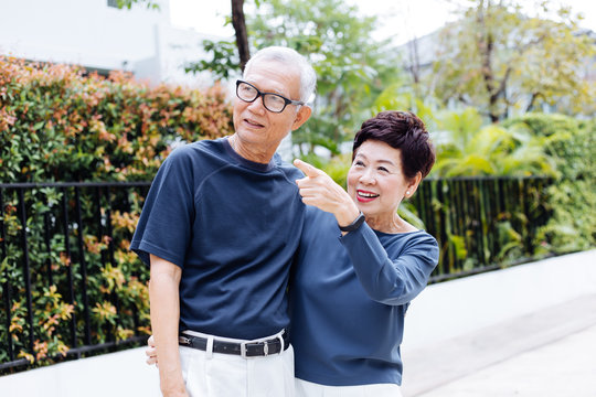 Happy senior Asian couple walking and pointing in outdoor park and house