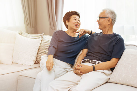 Romantic senior Asian couple laughing and sitting on sofa at home