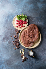 Ingredients for homemade sweet dessert chocolate pizza. Cocoa flat bread, different chocolates, raspberries, mint, jug of cream served on ceramic plates over blue texture background. Top view, space.