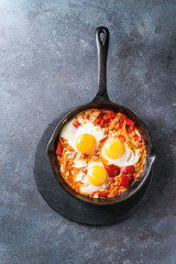 Traditional Israeli Cuisine dishes Shakshuka. Fried egg with vegetables tomatoes and paprika in cast-iron pan on wooden board over blue texture background. Top view, space.