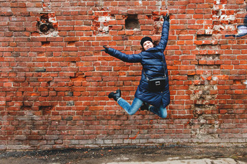 Fototapeta na wymiar smiling girl was photographed in a jump on a brick wall background