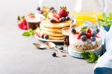 Oatmeal granola with berries and yogurt and panccakes on light gray concrete background. Healthy breakfast food concept with copy space.